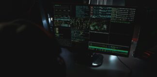 Ciemne biuro z monitorami pokazującymi kod związany z cyberbezpieczeństwem