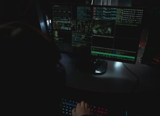 Ciemne biuro z monitorami pokazującymi kod związany z cyberbezpieczeństwem