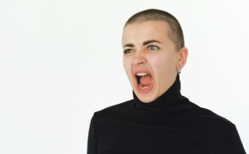 Kobieta w czarnym golfie krzyczy, wyrażając silne emocje