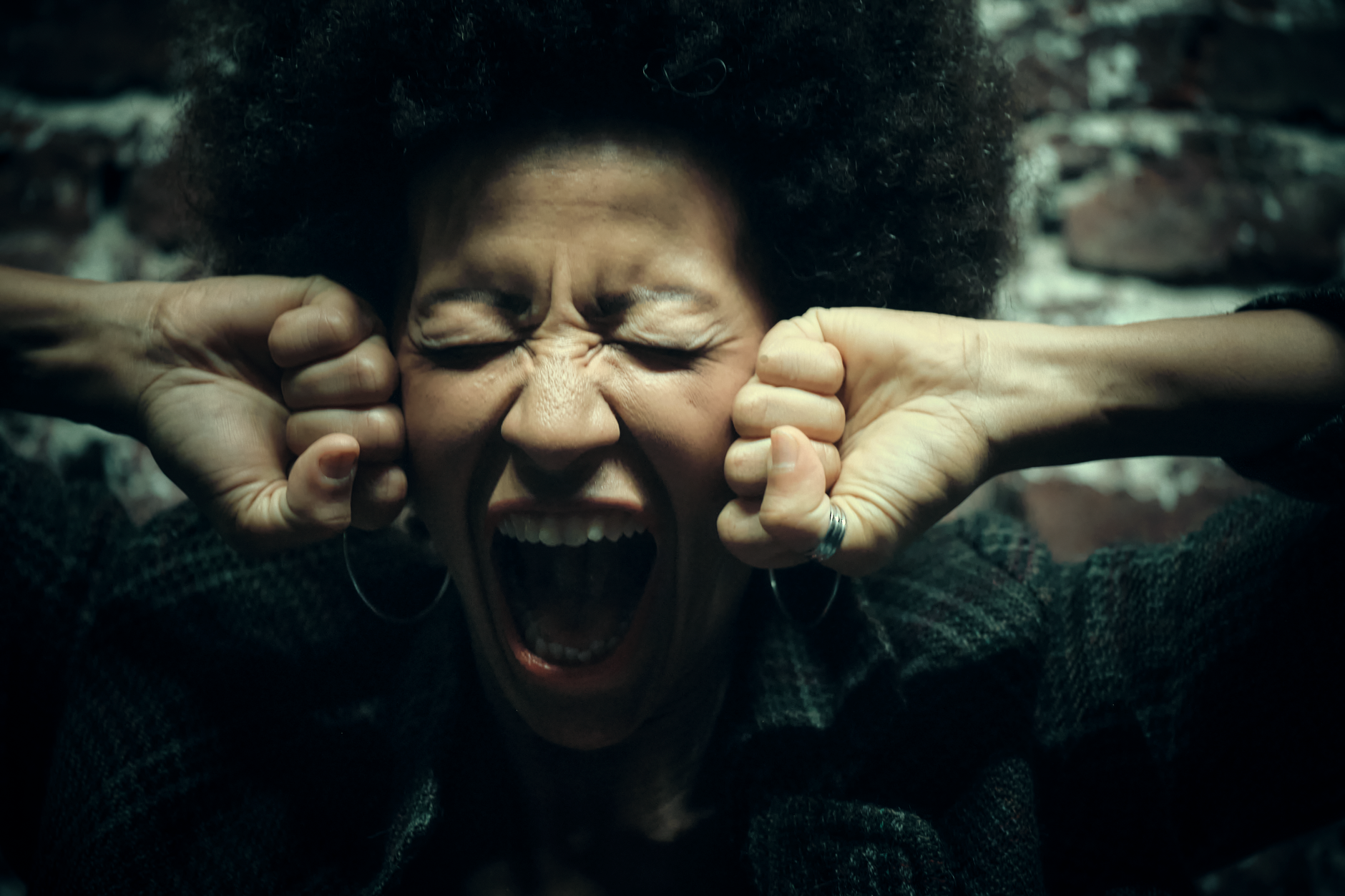 Zbliżenie kobiety z afro, która krzyczy z silnym gniewem przy ceglanej ścianie
