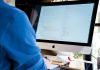 Programista w niebieskiej koszuli koduje na iMacu nad backendem Node.js