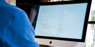 Programista w niebieskiej koszuli koduje na iMacu nad backendem Node.js