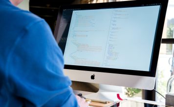 Programista w niebieskiej koszuli koduje na iMacu nad backendem Node.js