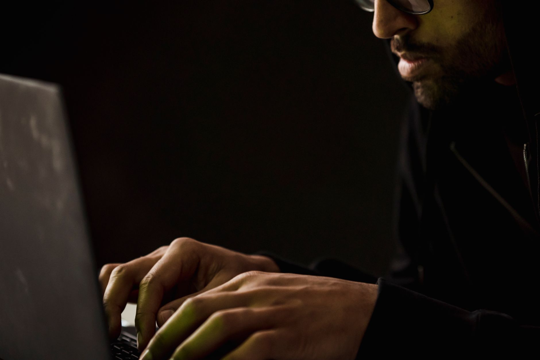 Brodaty mężczyzna w okularach przegląda netbook w ciemnym pokoju