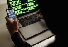 Haker w czarnej bluzie korzysta z netbooka i telefonu w biurze