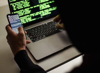 Haker w czarnej bluzie korzysta z netbooka i telefonu w biurze