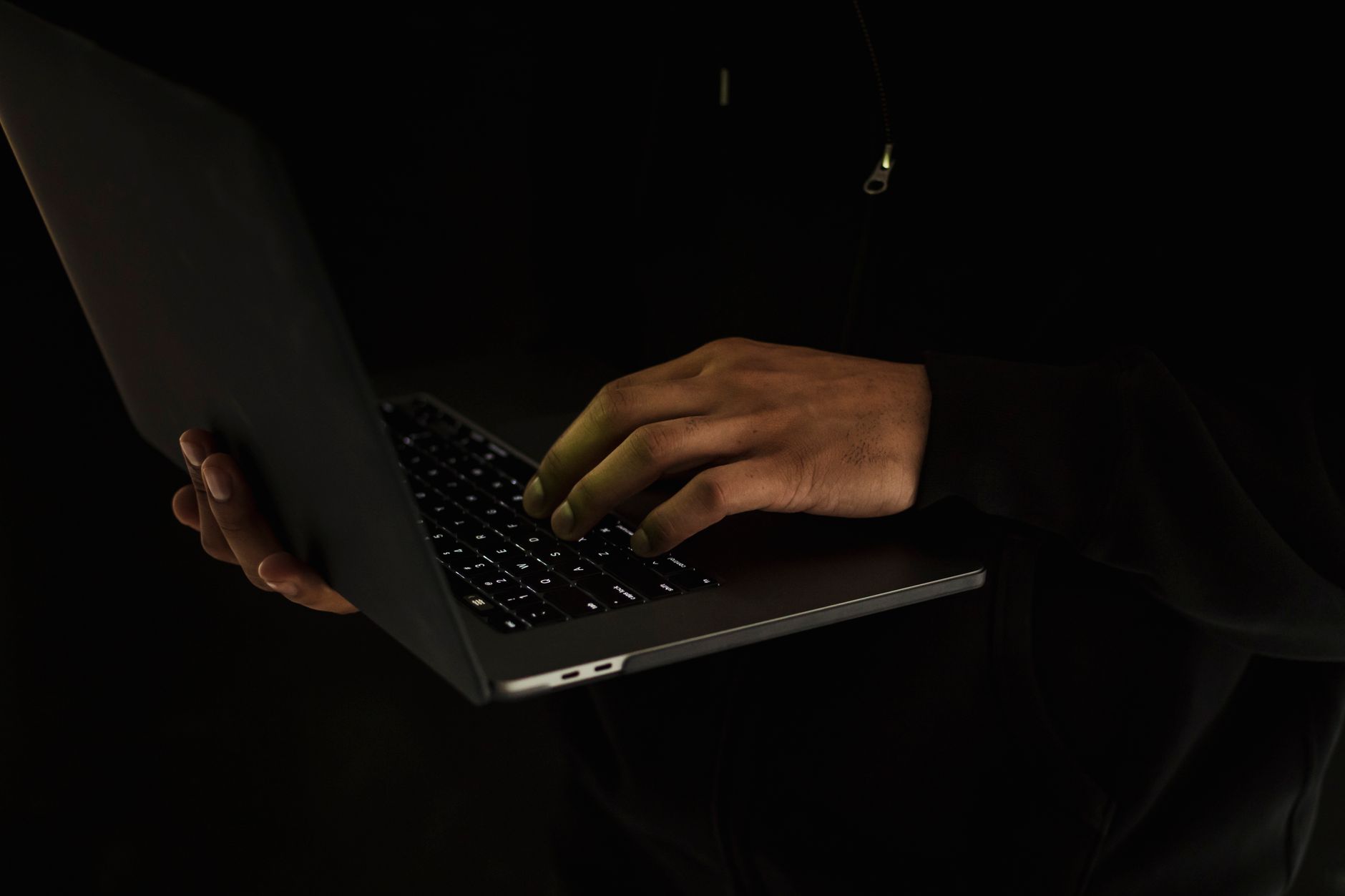 Mężczyzna w czarnym stroju z netbookiem w ciemnym pomieszczeniu